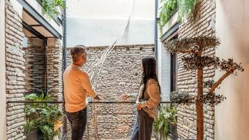 Un espacio interior estrecho con paredes de piedra, barandilla de cristal y plantas en macetas.