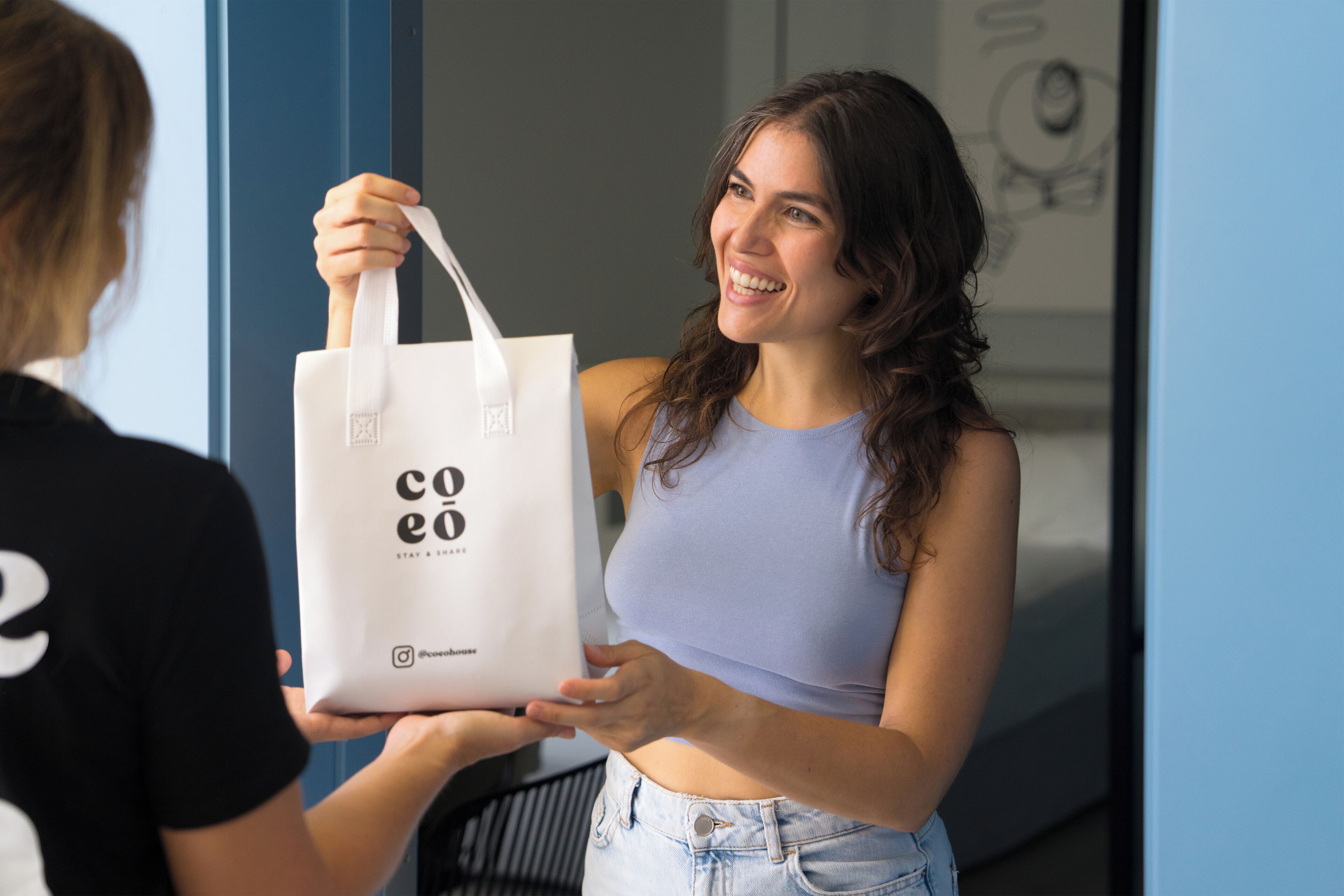 A person holding a white tote bag with 'coeo' branding.