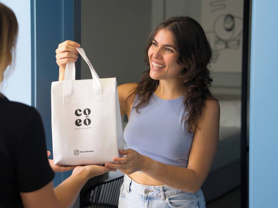 A person holding a white tote bag with 'coeo' branding.