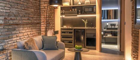 A modern living room with a brick wall, a grey sofa, a black floor lamp, and a small wooden table with apples.