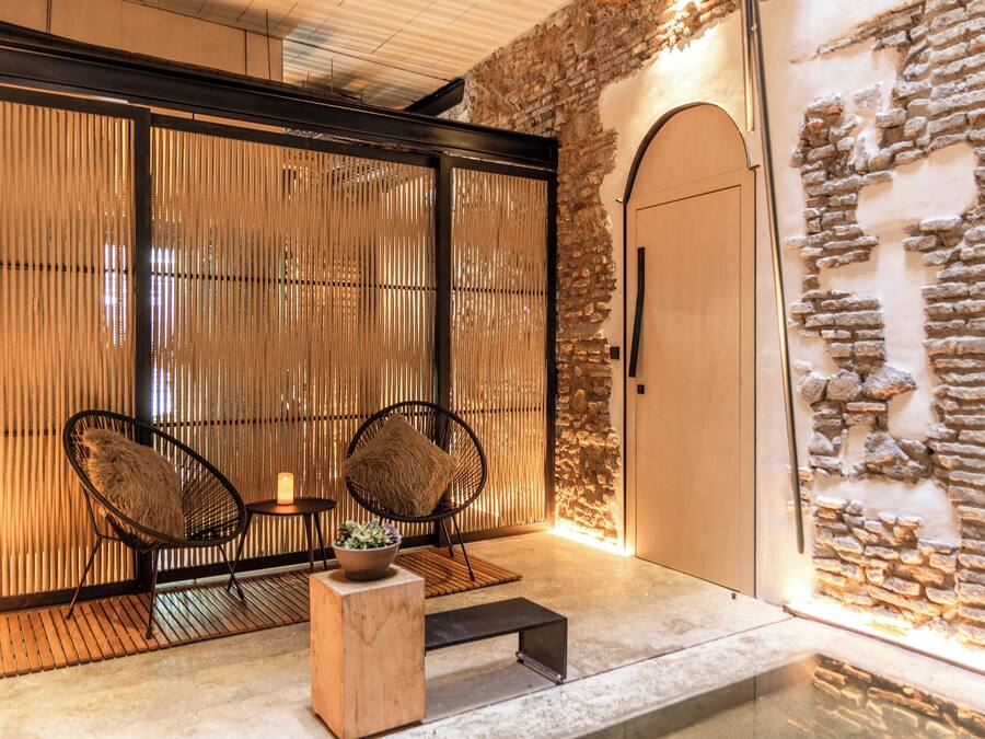 Una habitación con pared de piedra, puerta de madera y dos sillones de mimbre con cojines.