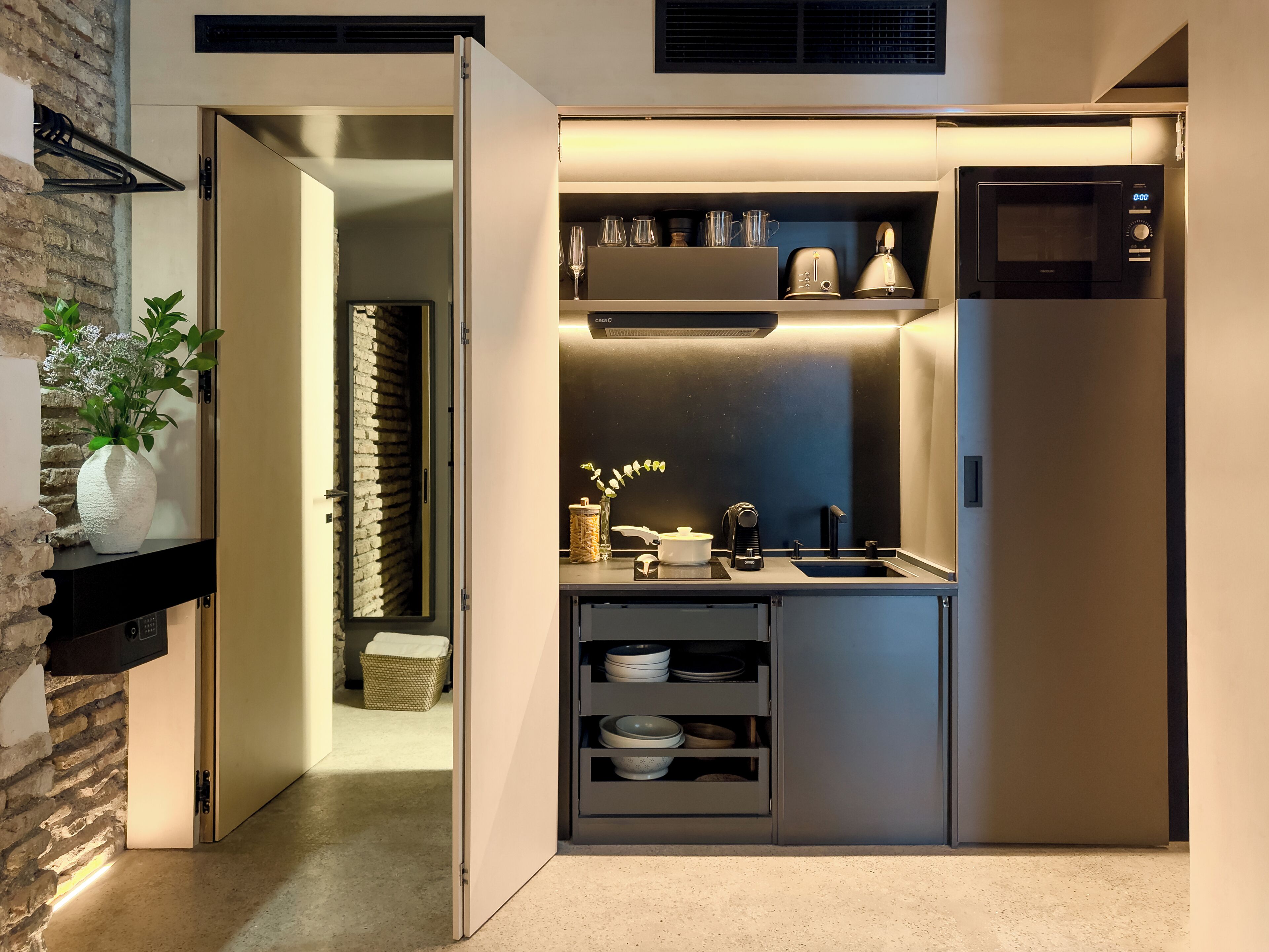 A compact kitchen with a microwave, toaster, and shelves for dishes.