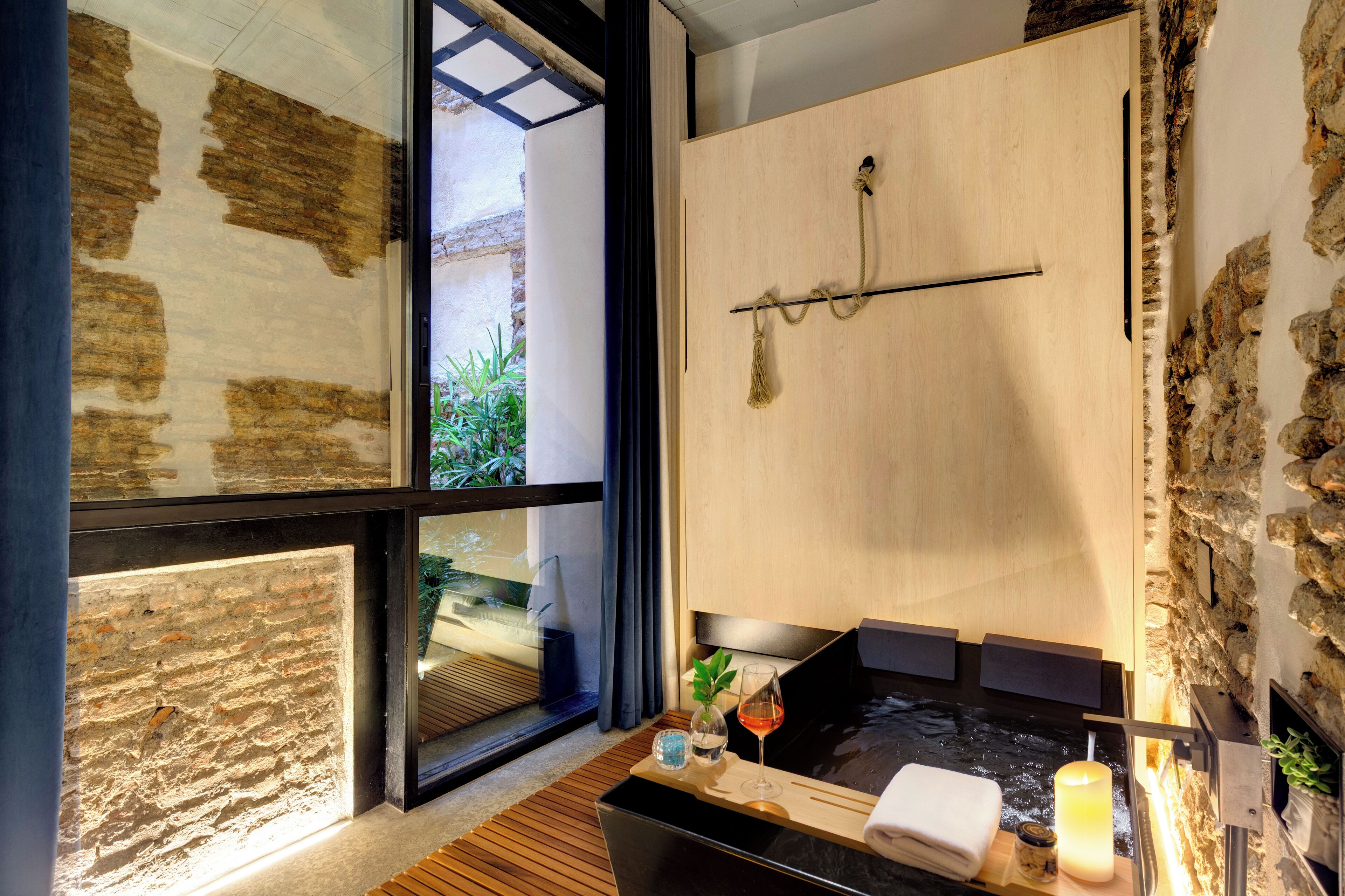 Un spa moderno con una bañera de madera, una puerta de cristal que da a un balcón y una pared de piedra.