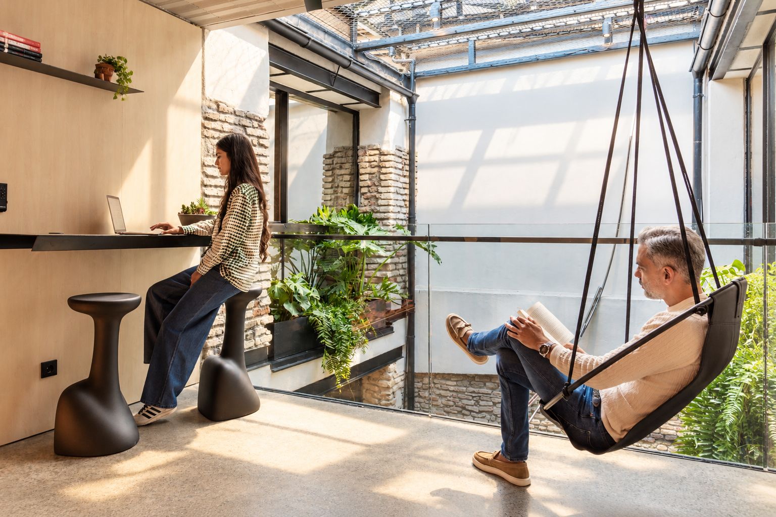 Un intérieur moderne avec un fauteuil suspendu, un bureau avec un ordinateur portable et une personne qui travaille.