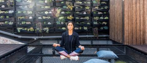 A person meditating on a rooftop with a garden wall behind.