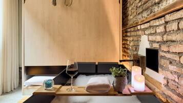 Un cuarto de spa con una camilla de madera, una copa de vino, una toalla, un jarrón con forma de rostro y una vela encendida.