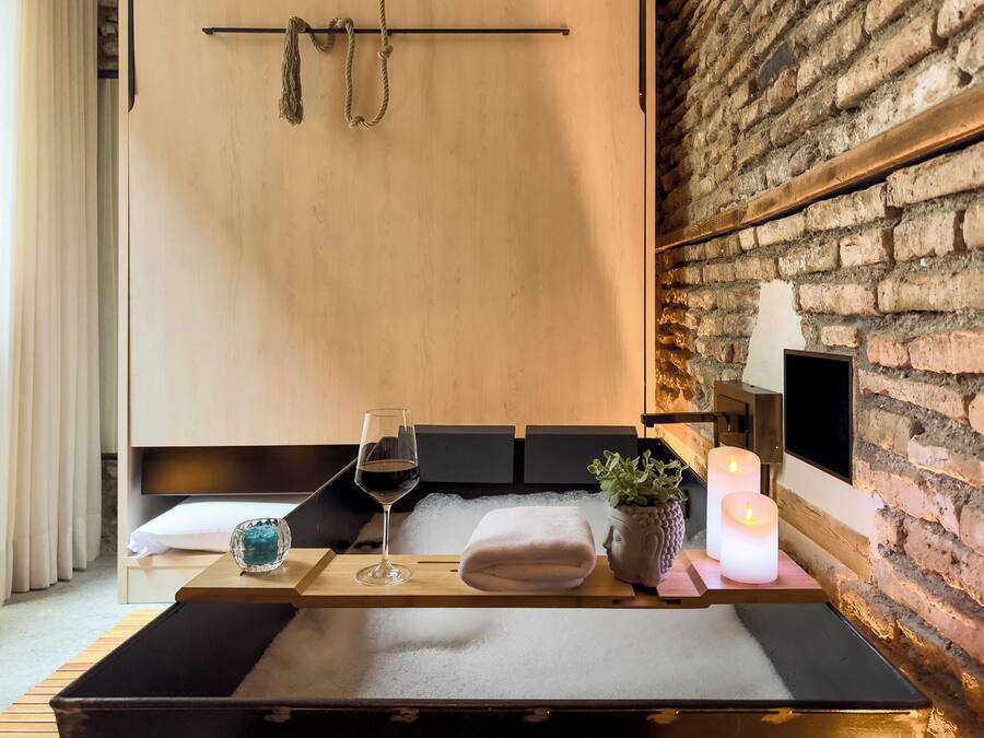 Un cuarto de spa con una camilla de madera, una copa de vino, una toalla, un jarrón con forma de rostro y una vela encendida.