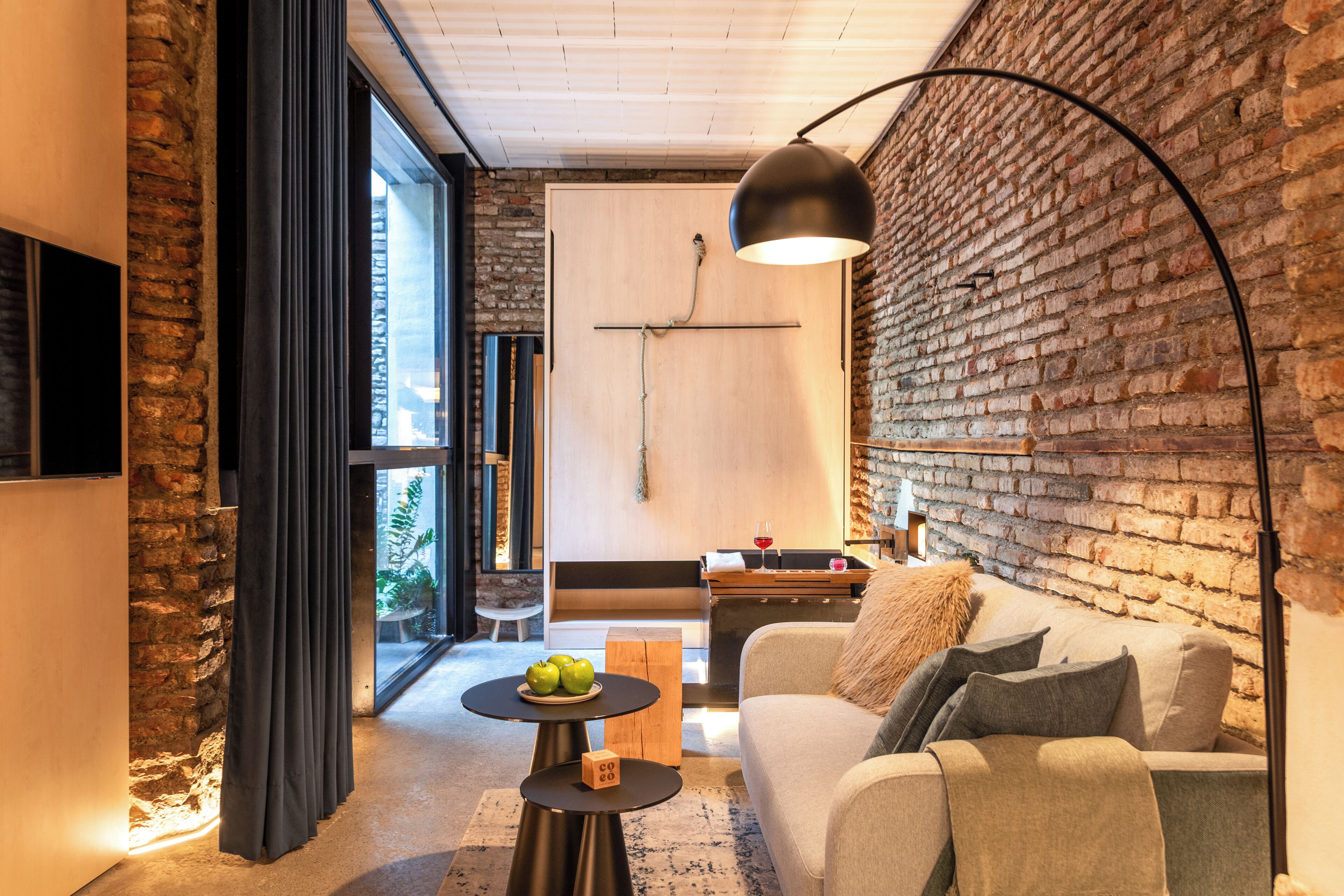 A modern living room with a brick wall, a sofa, a coffee table with apples, and a pendant light.