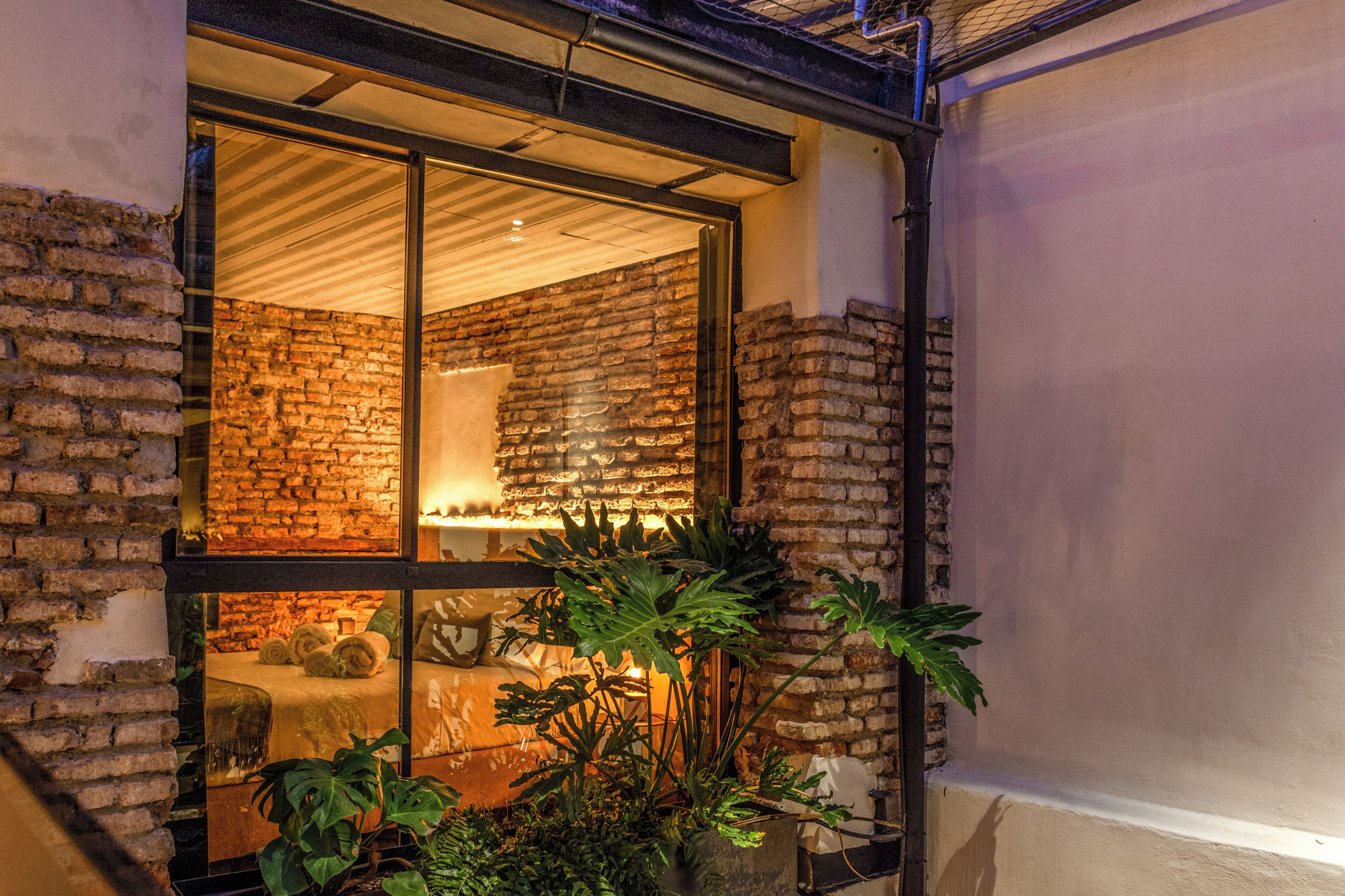 Una habitación con pared de ladrillo, un ventanal grande y una planta en primer plano.