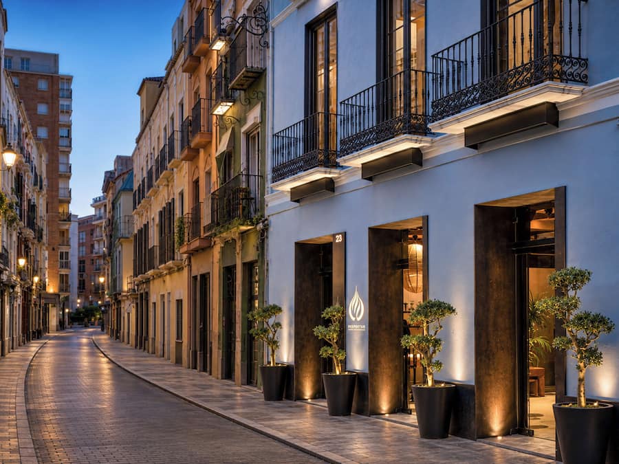 A hotel corridor with multiple doors, potted plants, and a clear view of the street.