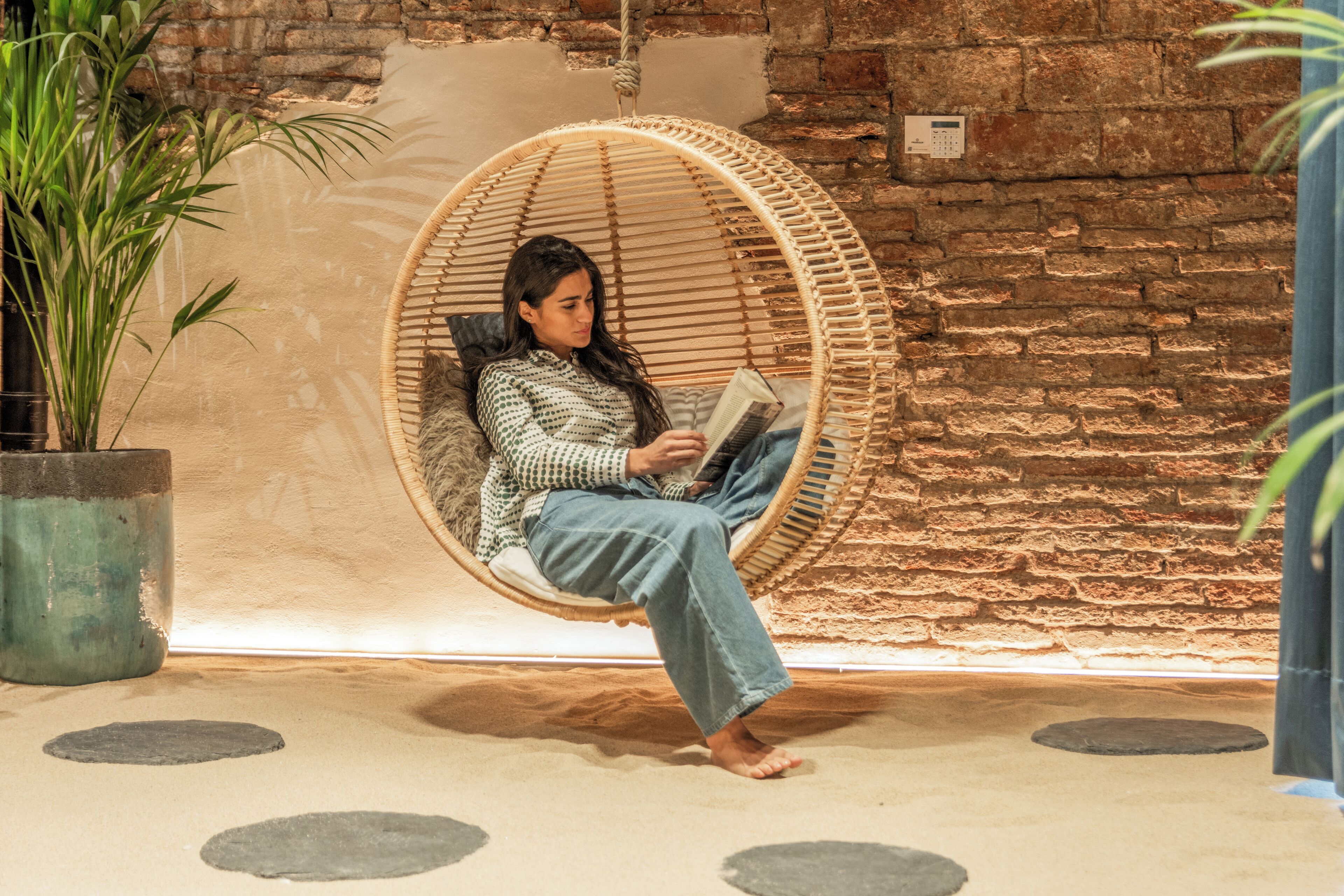 A person sitting in a circular wicker chair reading a book.