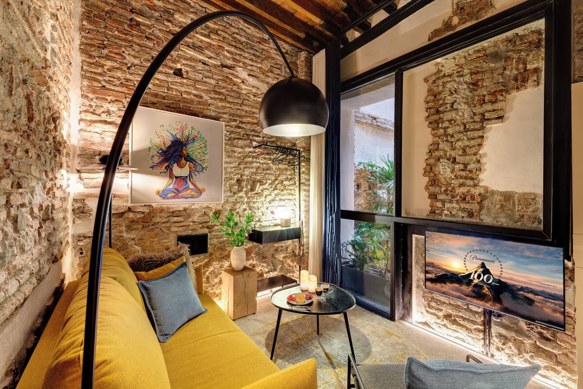 A cozy living room with a yellow sofa, a black floor lamp, and a large TV screen displaying a mountain scene.