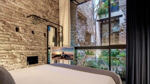 Un dormitorio moderno con una cama grande, una pared de ladrillo, una ventana con vistas a la vegetación y un cuadro de un atardecer.