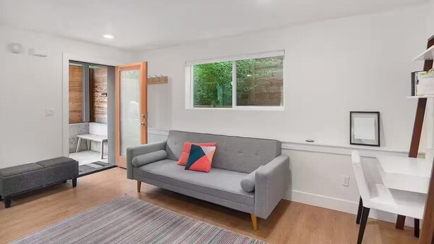 Un salon moderne avec un canapé gris, un petit banc et une table blanche.