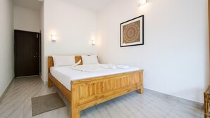 Une chambre à coucher avec un lit en bois, du linge de lit blanc, un petit tapis et un luminaire fixé au mur.