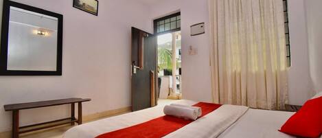 A hotel room with a bed, a bench, a door, and a window with curtains.