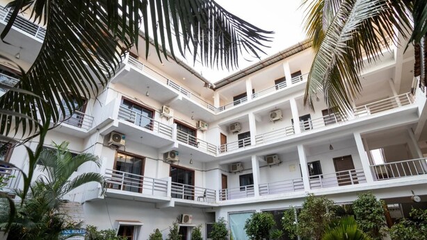 Un immeuble à plusieurs étages doté de balcons, de climatiseurs et d’un espace piscine agrémenté de palmiers.