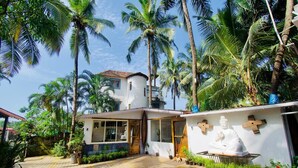 Un bâtiment blanc avec un toit en tuiles, entouré de palmiers et de plantes en pot.