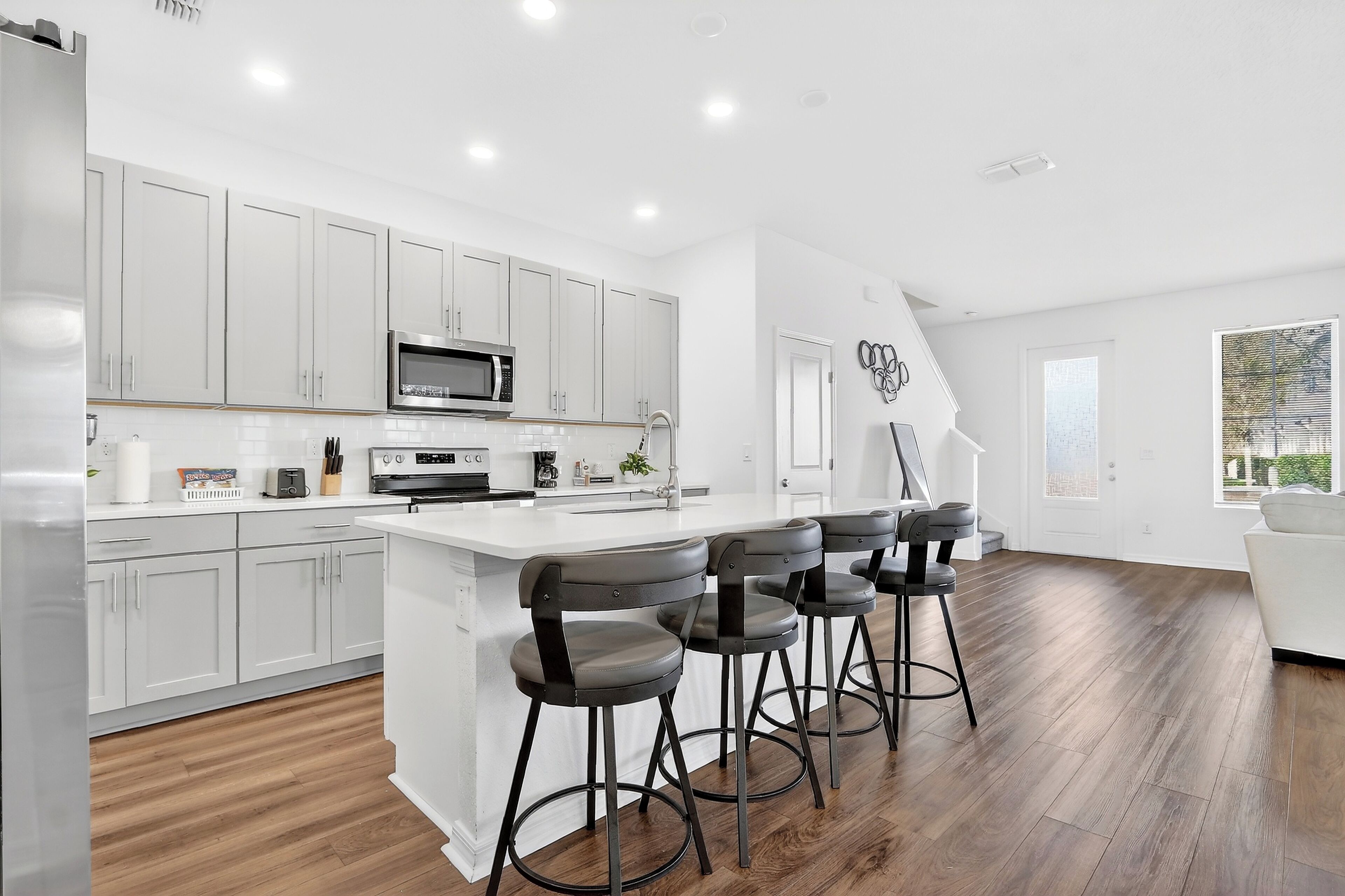 A modern kitchen with white cabinets, a central island with bar stools, and a large window providing natural light.