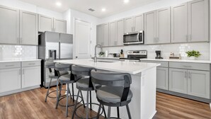 Une cuisine moderne avec des meubles gris, des appareils en acier inoxydable et un îlot central doté de tabourets de bar.