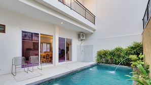 A modern indoor pool area with a clear view of the pool, two chairs, a table, and a balcony. - Villa Taman Seminyak 52 - Seminyak (Seminyak)