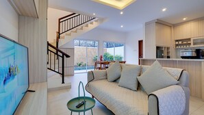 A modern living room with a sofa, TV, and a staircase leading to a balcony. - Villa Taman Seminyak 52 - Seminyak (Seminyak)