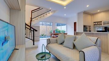 Una sala de estar moderna con un sofá, televisor y una escalera que lleva a un balcón.