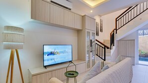 A modern living room with a flat-screen TV, a sofa, a lamp, and a staircase. - Villa Taman Seminyak 52 - Seminyak (Seminyak)