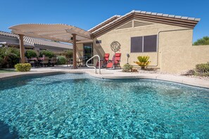 A clear swimming pool with a sunshade structure, red lounge chairs, and a building with a logo. -  Optional heated pool- 3-bedroom house in peaceful Surprise with AC (Surprise)