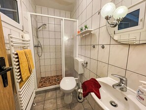 Un baño con ducha, inodoro, lavabo y un perchero con una toalla amarilla.
