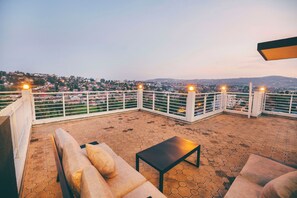 Eine Dachterrasse mit Blick auf eine Stadtlandschaft, inklusive Sofa, Tisch und Geländer.