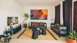 A living room with a sofa, two round tables, a TV, and a large painting on the wall. - THE TERRACE TOWNOUSE, a Creative Escape in the Heart of Kigali (Kigali)