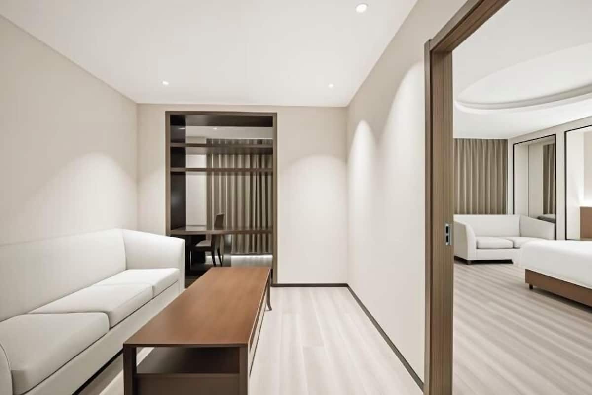 A modern hotel room with a white sofa, a wooden table, a mirror, and a built-in closet.