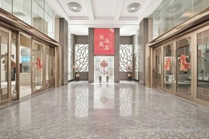 Un vestíbulo de hotel con piso de mármol, puertas de madera tradicionales y un banderín rojo.
