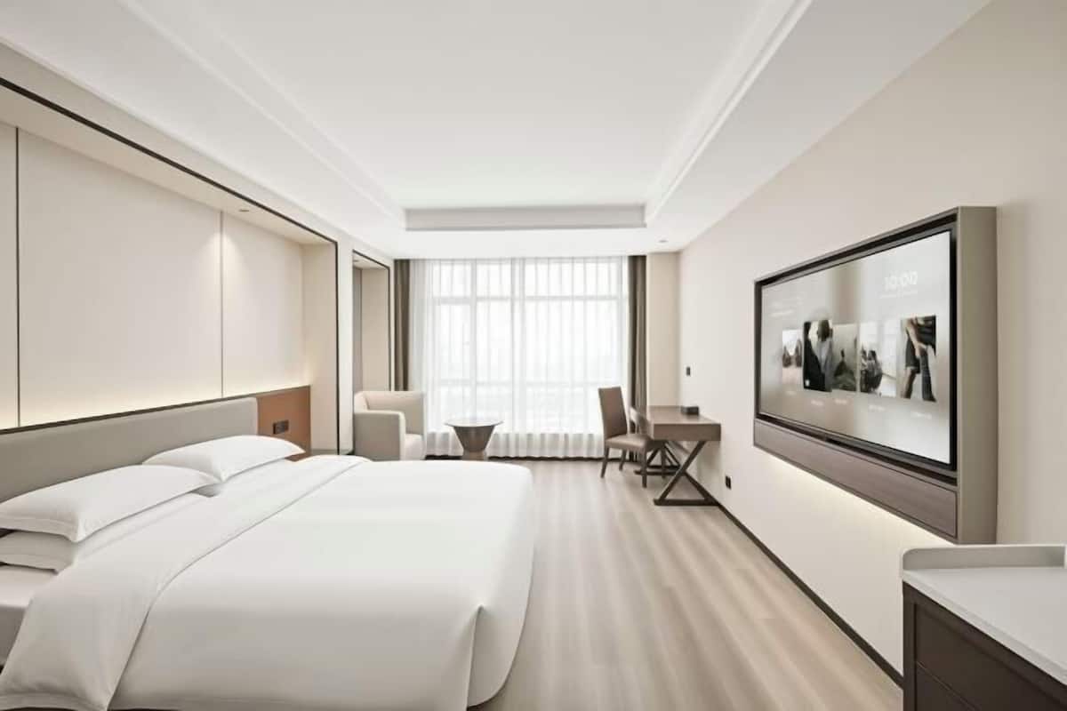 A modern hotel room with a large bed, a desk, a chair, and a television mounted on the wall.