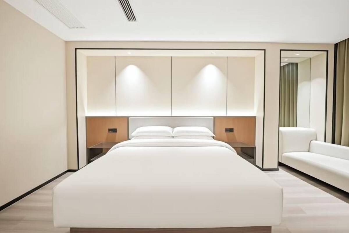 A modern hotel room with a large bed, a sofa, and a mirror.