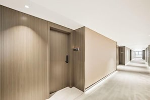 A modern hotel corridor with wooden panel walls, a carpeted floor, and a visible elevator. - Lanting Hotel (Danyang)
