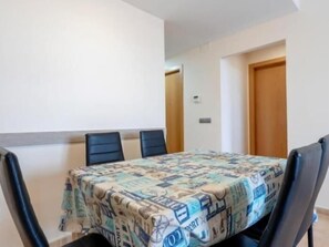 Un comedor con una mesa cubierta por un mantel estampado, cuatro sillas negras y una puerta de madera al fondo.