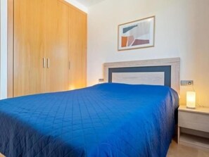 Un dormitorio con cama, mesita de noche, armario de madera y un cuadro enmarcado en la pared.