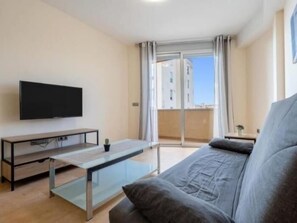 Una sala de estar moderna con un televisor de pantalla plana, una mesa de centro de vidrio y un sofá gris.