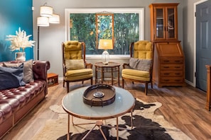 A living room with a leather sofa, two armchairs, a glass coffee table, a cabinet, and a window with a view of trees.