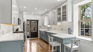 Une cuisine moderne dotée d’un îlot central, de meubles blancs et d’une grande fenêtre offrant une vue sur l’extérieur.