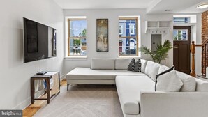 Un salon moderne doté d’un grand canapé d’angle, d’un téléviseur à écran plat fixé au mur et de grandes fenêtres offrant une vue sur la ville.