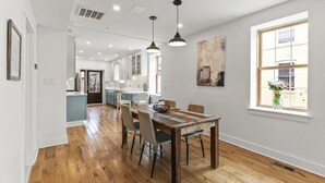 Un vaste espace dédié à la salle à manger, avec une table et des chaises en bois, une grande fenêtre offrant une belle vue et une cuisine en arrière-plan.