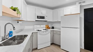 Een moderne keuken met witte kasten, een roestvrijstalen spoelbak, een magnetron, een fornuis en een koelkast.