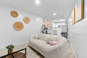 A modern living room with a beige sofa, a glass coffee table, and a potted plant. There are woven wall hangings and framed pictures on the wall. - Slice of the good Life: Concord A8 (Peoria)