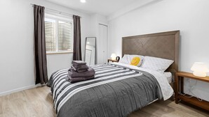 Een moderne slaapkamer met een groot bed, een nachtkastje, een spiegel en een raam met gordijnen.