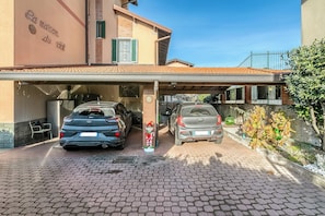A parking area with two cars parked under a covered structure. - Bee Apartment: Luino Lakeside With Outdoor Dining (Luino)