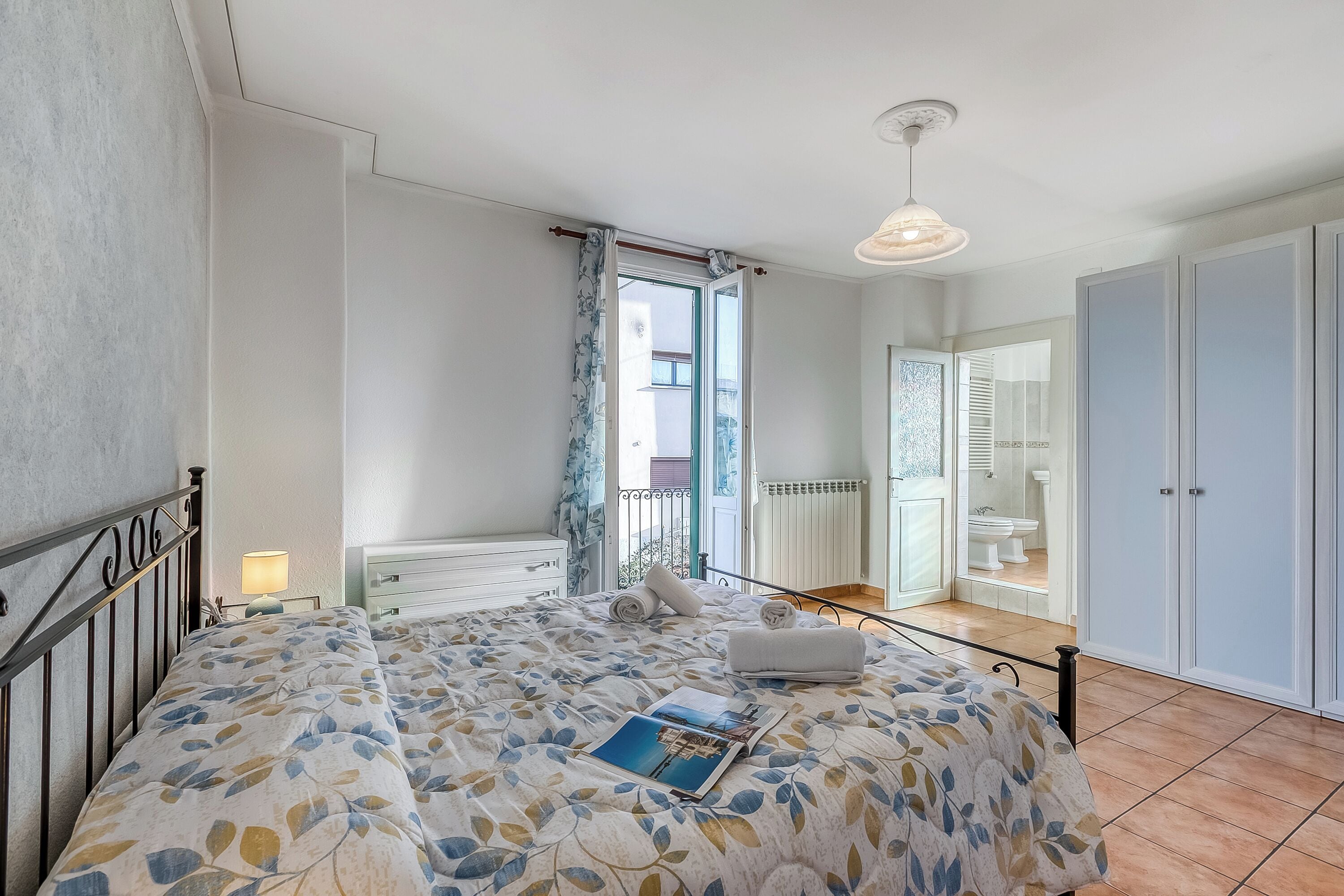 Una camera da letto con un letto, un comodino, una lampada, una finestra con tende e vista sull'esterno.