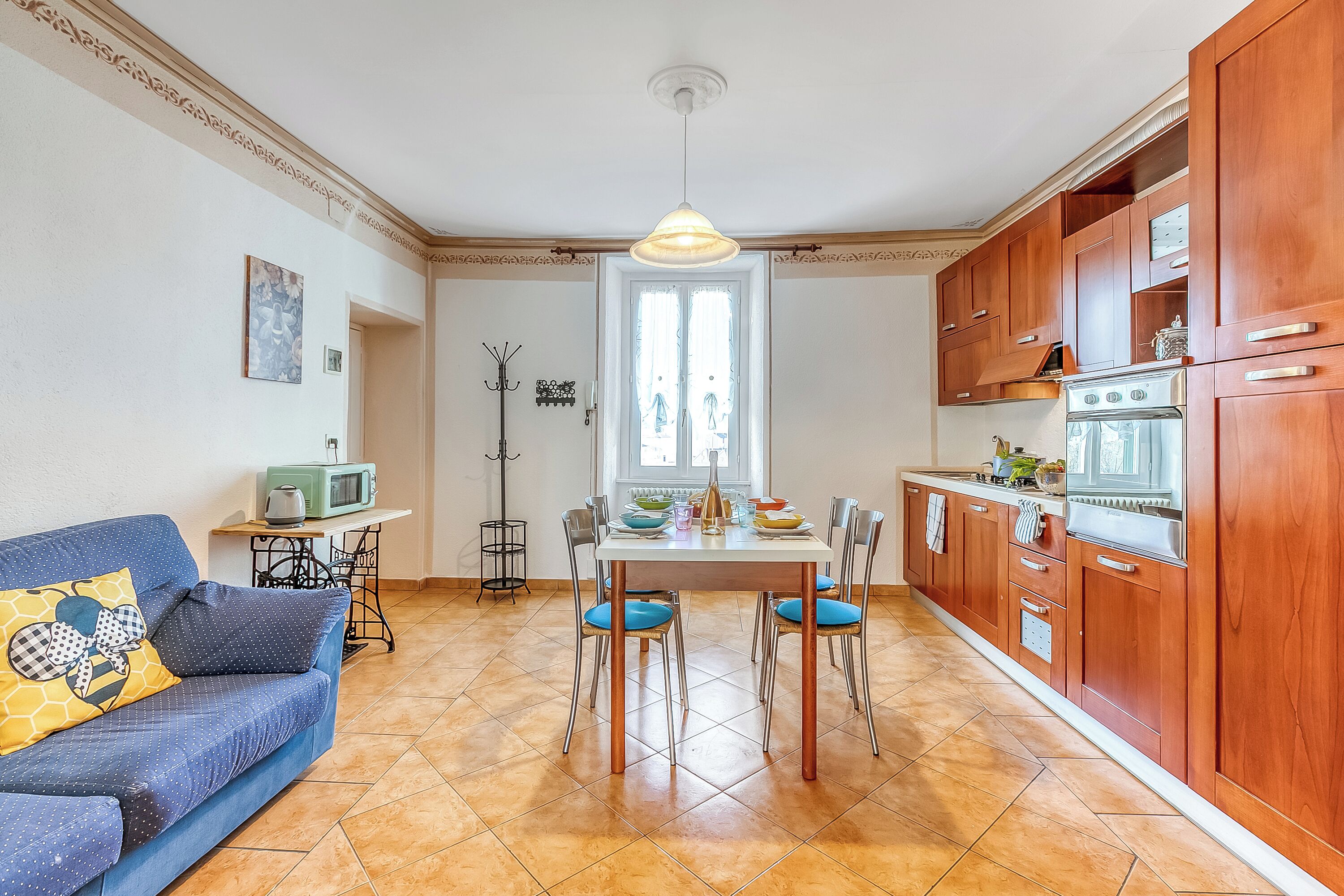 Una cucina compatta con mobili in legno, un tavolo da pranzo con sedie, un divano con cuscini decorati e una macchina da cucire nell'angolo.